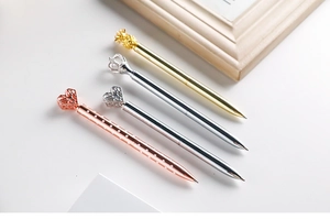 Detail of metal ballpoint pens with crown and heart toppers in gold and silver finish