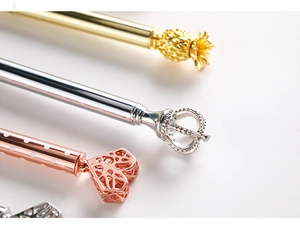 Detail view of gold and rose gold metal pens with crown, pineapple, and heart tops