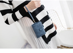 Detail of blue matte leather wallet with wrist strap held by a model in a cozy setting