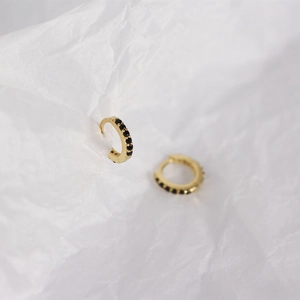 Macro shot of gold silver hoop earrings with small black gemstones on textured white background
