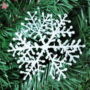 Close-up of white glitter snowflake ornament on green pine needles for Christmas decor