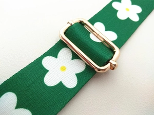 Close-up of adjustable green floral strap with white flower patterns and golden metal buckle