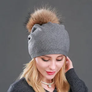 Berretto in maglia di lana grigia con grande pompon in pelliccia indossato da modella