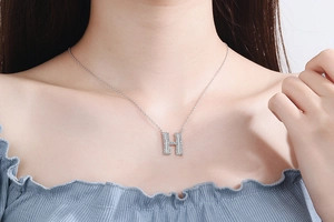Close-up of a silver-tone necklace featuring a sparkling crystal-encrusted letter H pendant