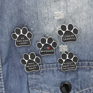 Set of 5 black paw print enamel pins with dog slogans on blue denim fabric
