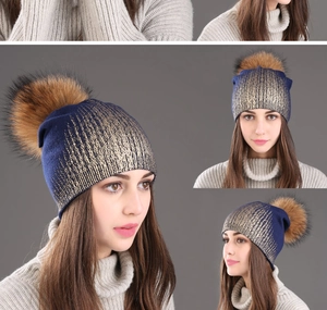 Detail view of navy knit winter beanie with gold foil texture and fluffy faux fur pompom