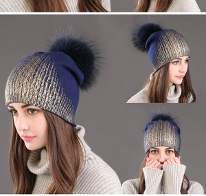 Detail view of navy blue knitted wool beanie with gold texture and fluffy fur pom-pom