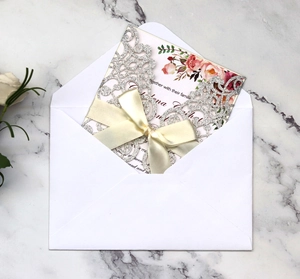 Detail of silver glitter laser cut wedding invitation with cream silk ribbon bow and rose