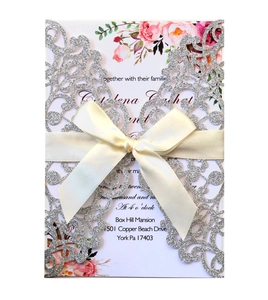 Laser-cut silver glitter wedding invitation with cream silk bow and floral patterns