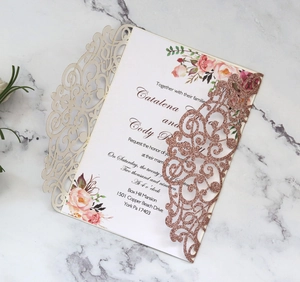 Detail of laser-cut glitter wedding invitation with floral insert on marble surface