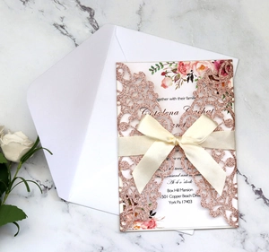 Detail of rose gold laser-cut wedding invitation with silk ribbon on marble background