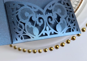 Close-up of laser-cut floral lace patterns on an elegant blue wedding invitation card