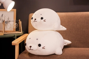 Detail of two white plush seal toys in small and large sizes stacked on a brown sofa
