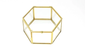 Close-up of a hexagonal clear glass ring box with polished gold metal frame on white background