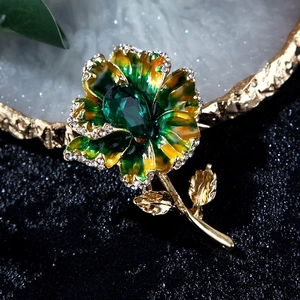 Detailed macro of flower brooch with green pear-shaped crystal and enamel petals