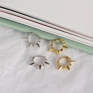 Detailed view of silver and gold punk spike hoop earrings on a textured white background