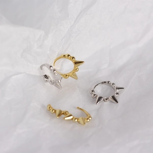Detailed view of silver and gold punk spike hoop earrings on textured background