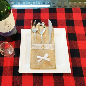 Lace-trimmed burlap Christmas cutlery holder with metal utensils on a red plaid tablecloth