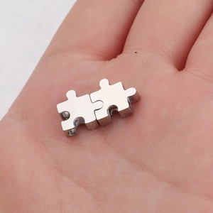 Pendentifs puzzle en acier inoxydable poli tenus en main montrant la taille miniature