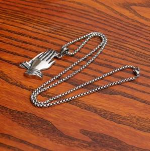 Detailed top view of silver stainless steel praying hands pendant on a wooden surface