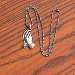 Macro detail of silver praying hands pendant and stainless steel box chain on wood