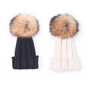 Warm children's knit beanies with oversized faux fur pom-poms in black and beige