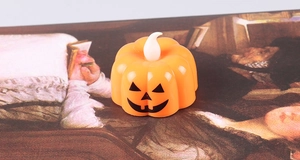 Detail view of orange LED pumpkin tea light with glowing flame and spooky face print