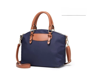 Oblique side view of navy oxford cloth handbag with brown leather straps and gold hardware