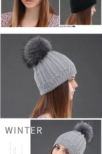 Detail of grey cable knit winter beanie featuring a large fluffy faux fur pom-pom topper