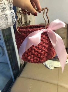Detail of red handmade crochet bag with golden cat ear handle and silk bow decoration