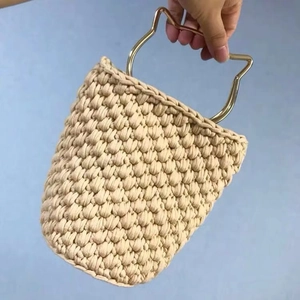 Detail view of the cat ear metal handle on a beige hand-woven bucket bag with golden hardware