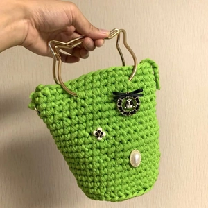 Detail of green crochet handbag featuring a golden cat-ear metal handle and floral decor