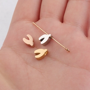Polished stainless steel wishbone beads in gold, silver, and rose gold on a palm