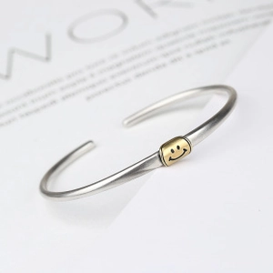 Detailed macro view of silver brushed bangle with a gold smiley face charm element