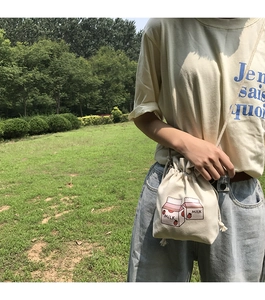 Detail of canvas drawstring bucket bag featuring cute strawberry milk illustration and strap