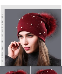 Detail of burgundy knitted winter hat with pearl beads, rhinestones and large fur pompom