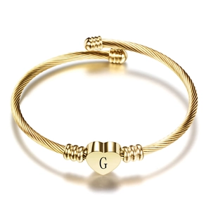 Macro shot of gold heart pendant with letter G on textured cable stainless steel bracelet
