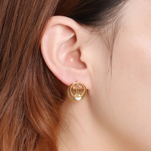 Golden hollow cross earring with clear crystal stone worn by a model in soft light