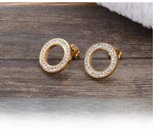 Detail of gold circular stud earrings featuring pavé set white crystals on a wooden surface
