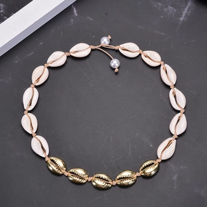 Natural shell necklace with golden accents and pearls on woven rope over dark marble