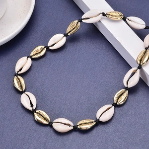 Golden alloy shell necklace with white beads and black cord on deep blue background