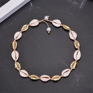 Macro view of woven necklace featuring gold and white shell beads on beige cord