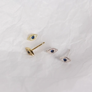 Macro shot of silver and gold evil eye stud earrings with blue stones and diamonds