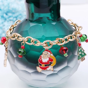 Macro shot of gold-tone Christmas bracelet with Santa and tree charms on a green glass bottle