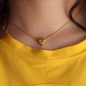 Golden heart pendant necklace with engraved letter A worn on a female model