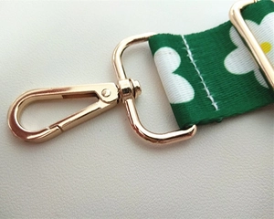 Detailed view of green daisy print bag strap with adjustable gold metal hardware