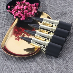 Elegant display of four black and gold lipstick tubes on a golden tray with pink flowers
