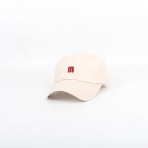 Close-up of red M letter embroidery on beige cotton baseball cap with curved brim