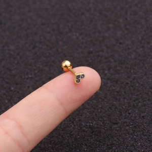 Close-up of a tiny gold heart-shaped stud earring with a blue zircon held on a fingertip
