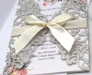 Detail of silver laser-cut wedding invitation with glitter finish and satin ribbon bow
